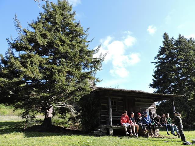 Image of a group of people sitting on the porch of a log cabin. 