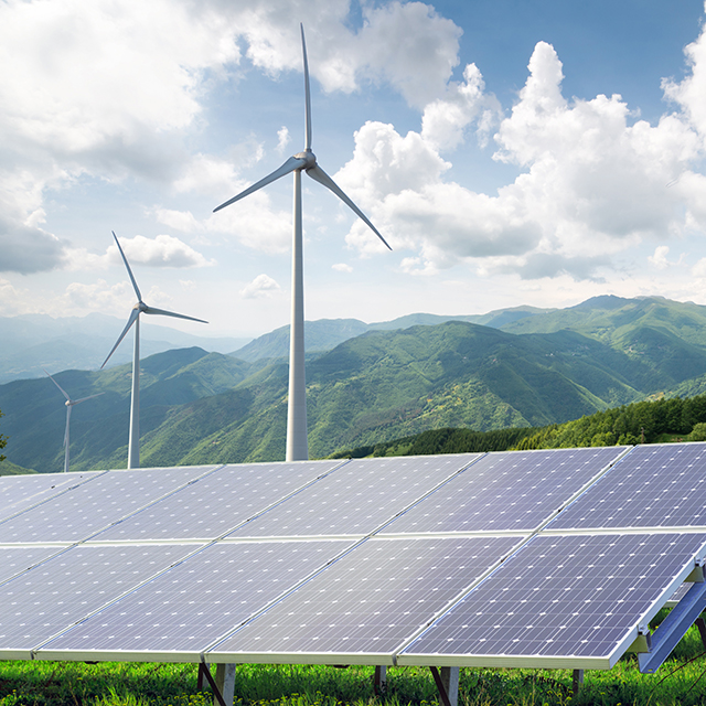 solar panels with wind turbines against mountains landscape against blue sky with clouds.