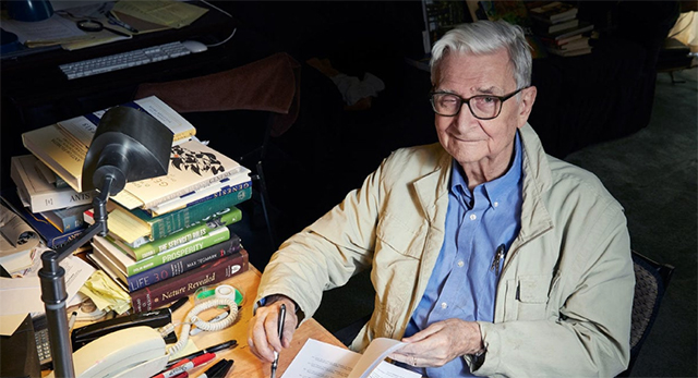 Image of E.O. Wilson sitting beside a stack of books.