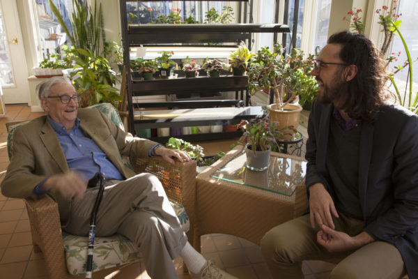 E.O. Wilson sitting in a chair and speaking to another man.