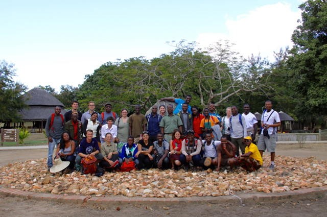 Image of a large group of students standing in from of a boulder.