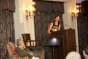 Image of a woman speaking on stage and E.O. Wilson sitting beside her.