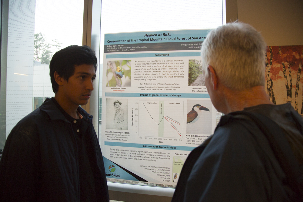 Image of a couple of men standing in front of a poster.